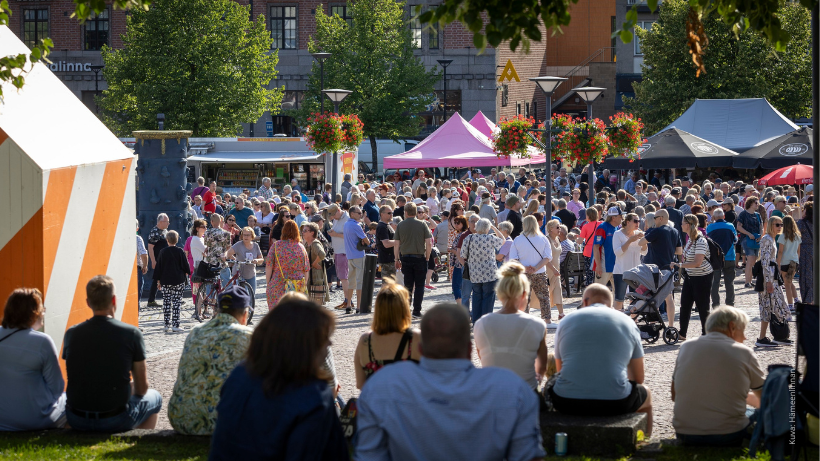 Vilkasta tapahtumatunnelmaa Hämeenlinnan keskustassa. Tapahtuma-alueella liikkuu runsaasti ihmisiä kojujen ja ohjelmapisteiden ympärillä.